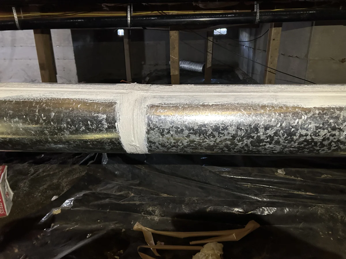 duct-sealing-img-1 Metal pipe with a white sealant joint in a basement/utility area, showing a recent repair.
